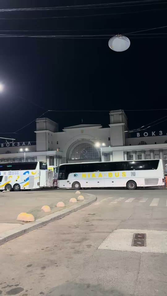 Білий бус уночі біля вокзалу, відчинені двері в салон із синім підсвічуванням