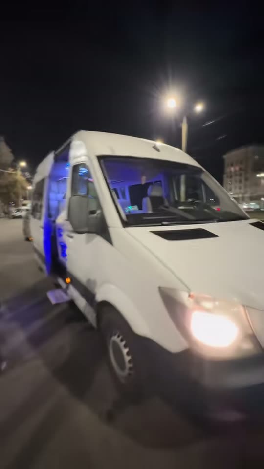 Білий бус уночі біля вокзалу, відчинені двері в салон із синім підсвічуванням